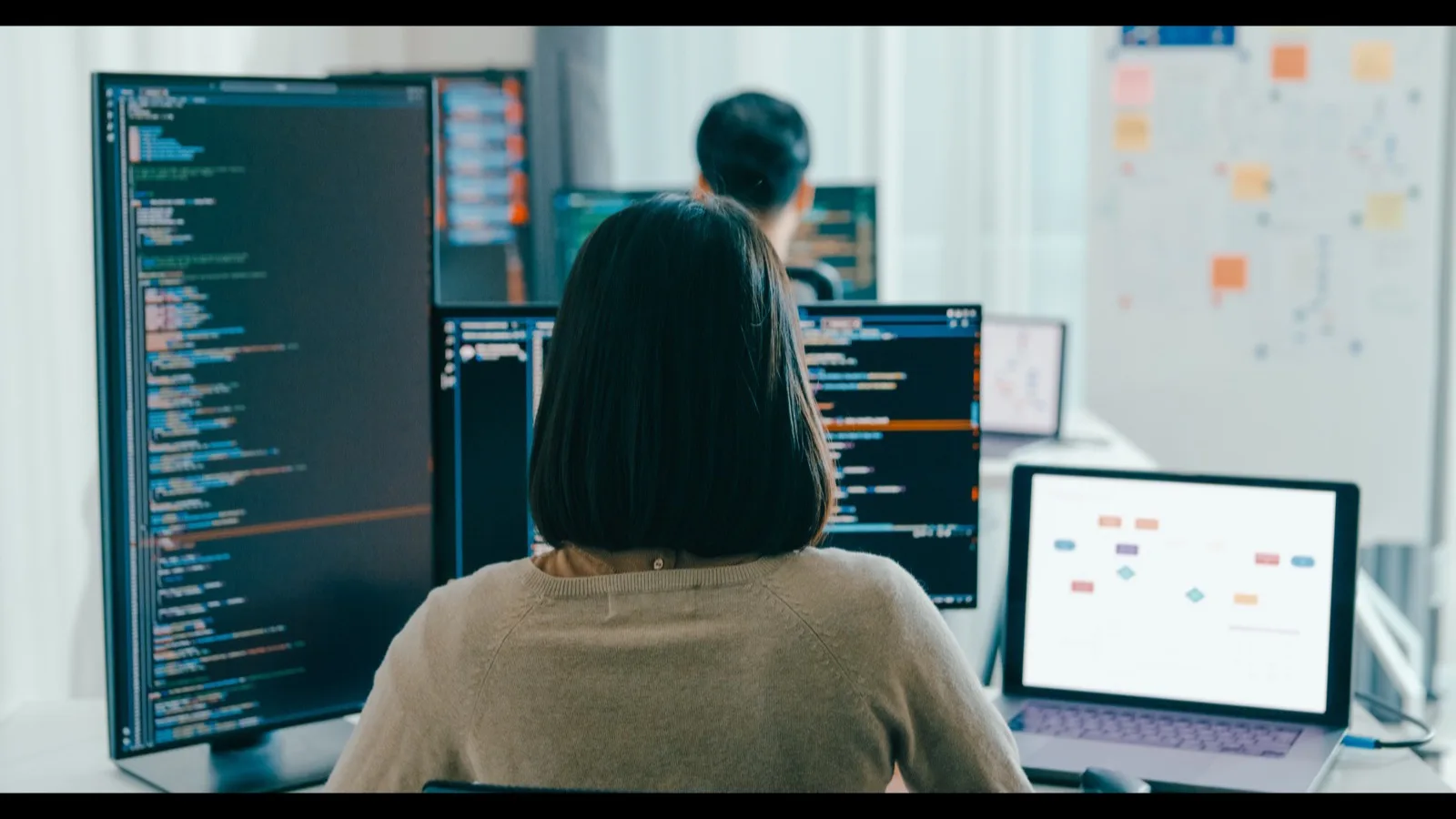 Software developer working with system architecture flowchart and code on multiple monitors