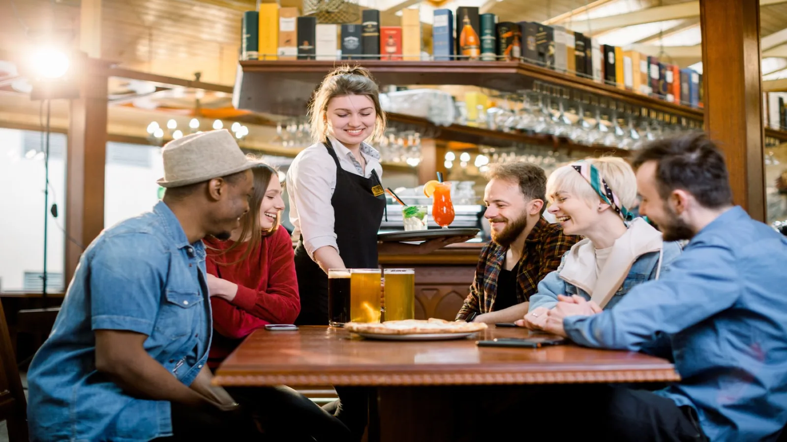 Server presenting beers and drinks to a group of friends at a busy US pub