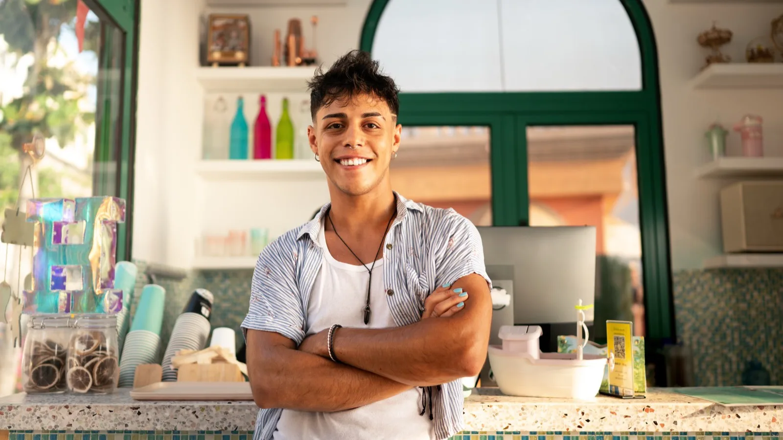 Young Hispanic small business owner standing confidently behind colorful storefront counter